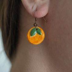 a close up of a person wearing earrings with an orange and green leaf on it