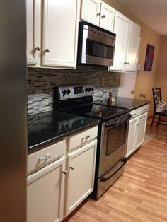 a kitchen with white cabinets and black counter tops, stainless steel appliances and wood flooring