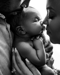 a black and white photo of a baby being held by his mother, who is kissing him