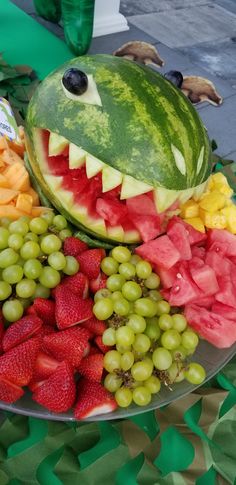 a watermelon shark face made out of fruit on a platter with grapes and strawberries