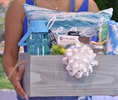 a woman holding a wooden box filled with items and water bottles on top of it