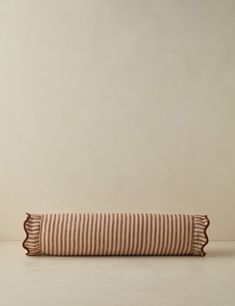 a brown and white striped pillow with ruffles on the bottom, in front of a beige wall