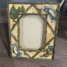 a decorative photo frame with birds and trees in the center on a wooden table top