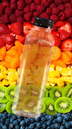 a plastic bottle filled with fruit sitting on top of a pile of blueberries, kiwis and strawberries