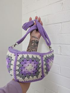 a hand holding a crocheted purse in front of a white brick wall with a tattoo on it