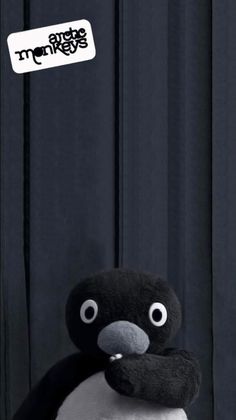 a stuffed penguin sitting on top of a wooden floor next to a black curtain with white lettering