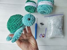 a hand holding a crocheted turtle next to some yarn and scissors on a table