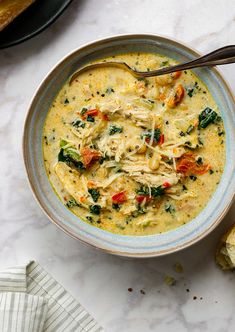 a bowl of chicken and spinach soup on a marble countertop next to slices of bread