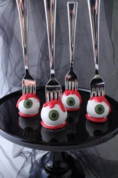 four forks with eyeballs on them are sitting on a black cake plate and one has three forks in the shape of eyes