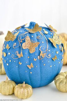 a blue pumpkin with gold butterflies on it sitting next to two small golden pumpkins