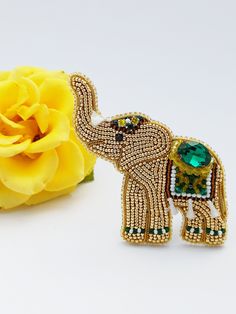 an elephant brooch sitting next to a yellow rose on a white surface with one flower in the foreground