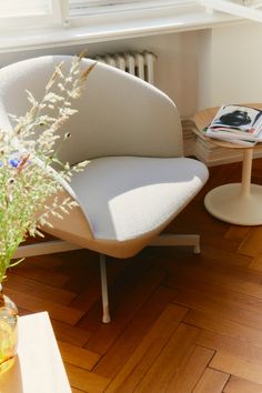 a white chair sitting on top of a hard wood floor next to a vase filled with flowers