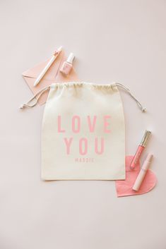 a white bag with the words love you on it next to some lipstick and brushes