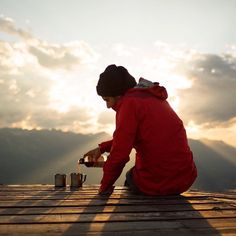 a man sitting on top of a wooden deck pouring something into a can with the sky in the background