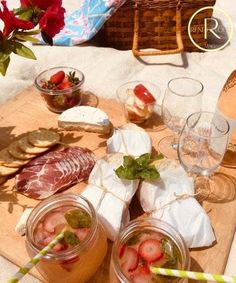 some strawberries and other food are on a wooden tray near glasses with strawberries in them