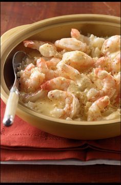 a bowl filled with shrimp and rice on top of a red cloth next to a spoon