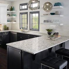 a kitchen with black and white cabinets, marble counter tops and stools in front of the island