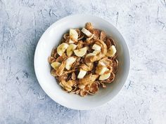 a white bowl filled with sliced bananas on top of a gray countertop next to a spoon