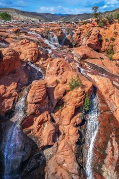 people standing at the top of a waterfall in an area that looks like it is surrounded by red rocks