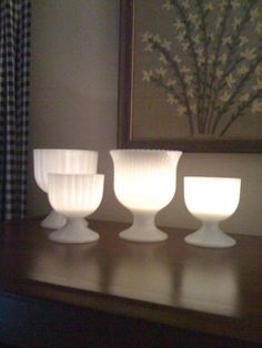 three white bowls sitting on top of a wooden table next to a framed painting and window