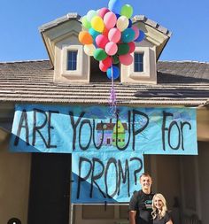 a man standing in front of a house holding a bunch of balloons with the words are you up for prom written on it