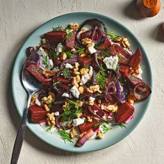 a white plate topped with beets, nuts and feta cheese on top of a table