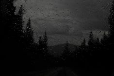 rain drops on the windshield of a car as it drives down a road in the dark