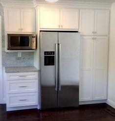 a silver refrigerator freezer sitting inside of a kitchen next to white cabinets and drawers