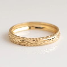 a gold wedding band with intricate designs on the sides and beaded edges, set against a plain white background