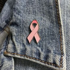 a pink ribbon pin sitting in the pocket of a pair of blue jeans on top of a denim jacket