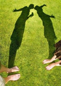 two people are standing in the grass with their shadows on them, and one person is holding