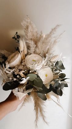 a bridal bouquet with feathers and flowers in someone's hand on the wall