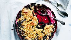 a blueberry pie with crumbled toppings on a white cloth next to a spoon