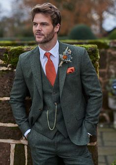 a man in a suit and tie standing next to a brick wall with moss growing on it