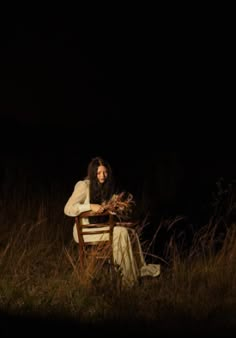 a woman sitting on top of a wooden chair in the middle of a grass field