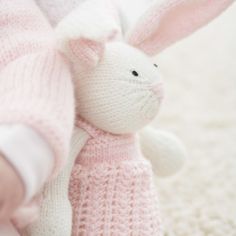 a stuffed rabbit in a pink sweater on the floor next to a baby's leg