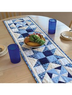 a table runner with blue glass vases and plates on it, along with a bowl of fruit