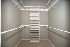 an empty walk in closet with white shelving and beige carpeted flooring on the walls