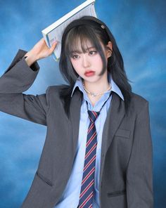 a woman with long black hair wearing a suit and tie holding a book over her head