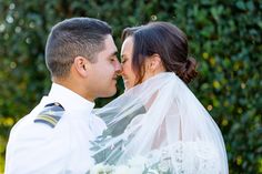 a bride and groom kissing under a veil in front of some green bushes at their wedding