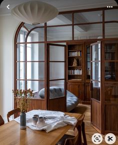 a wooden table sitting in front of a window next to a book shelf filled with books