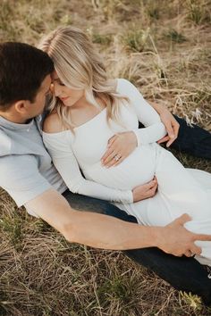 a pregnant couple cuddle while sitting on the ground