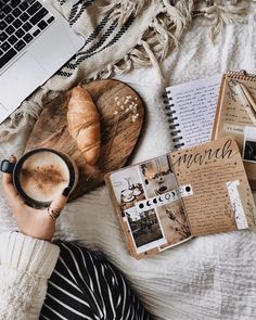 a person holding a cup of coffee next to a notebook and croissant