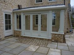 a house that has some doors and windows on the side of it with stone flooring