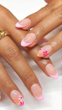 a woman's hands with pink and orange nail polishes on her nails, holding a gold ring