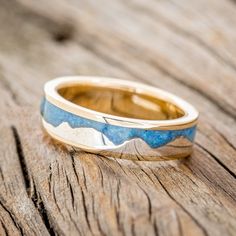 a gold and blue wedding ring sitting on top of a wooden table next to a piece of wood