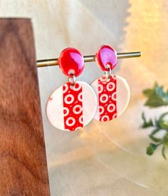 two red and white earrings are hanging from a wooden stand next to a green plant