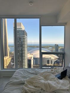 an unmade bed is in front of large windows overlooking the water and cityscape