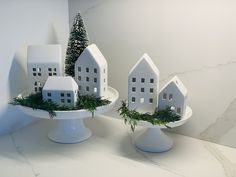 three white houses are sitting on plates with evergreen sprigs