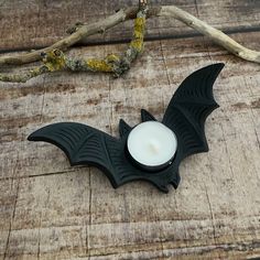 a candle that is next to a bat shaped candle holder on a wooden surface with branches in the background